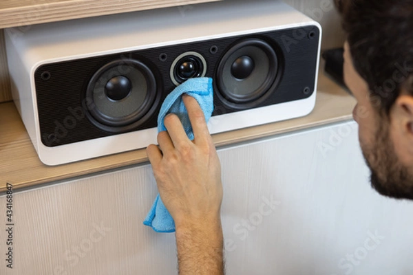 Fototapeta An unrecognizable Caucasian man does a wet cleaning, dusting a musical speaker system. Spring cleaning concept, hygiene in the house, changing roles in the family. Soft selective focus