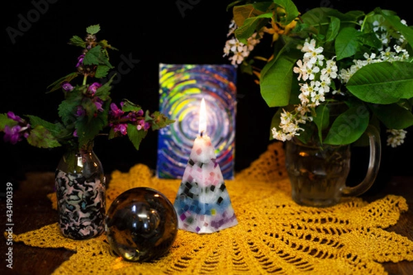 Obraz Still life with a burning candle, a vase with white flowers, purple conditions and a glass ball