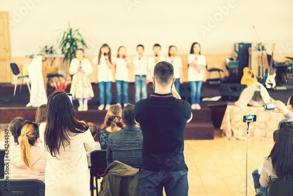 Fototapeta Children on the stage. Children on stage perform in front of parents. Young talents on stage. Children stand in front of parents in school. Blurry. toned