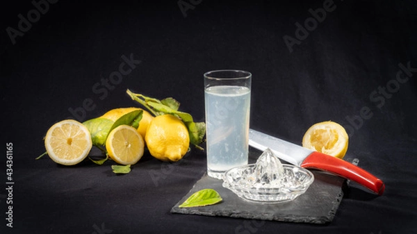 Fototapeta Freshly squeezed lemon juice placed on a slate with its citrus press and yellow lemons on a black background