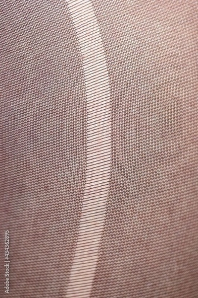 Fototapeta A closeup macro portrait of the texture of a rip, tear, run, ladder in the fabric of black nylon stockings, pantyhose. The pattern of the threads is wider apart at the rip.