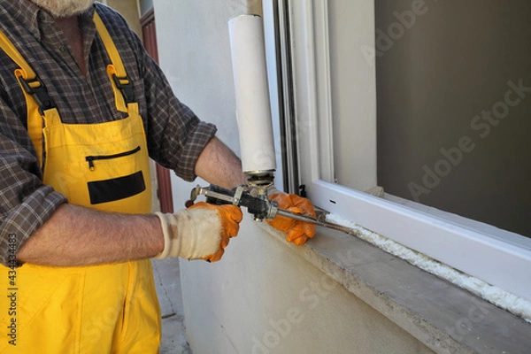 Fototapeta Worker installing new plastic window, using handgun with polyurethane foam 