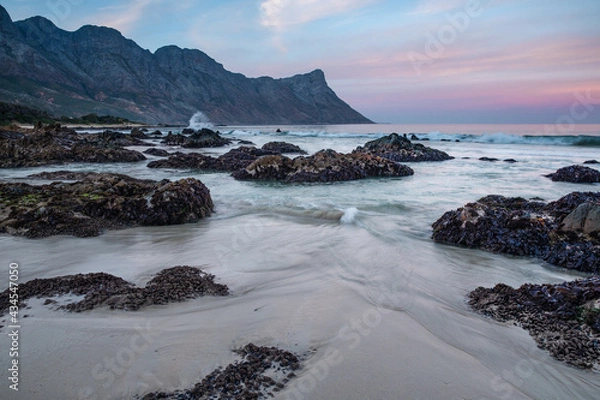 Fototapeta Landscape photo of mountain range ending in the ocean with rocks and ocean in foreground