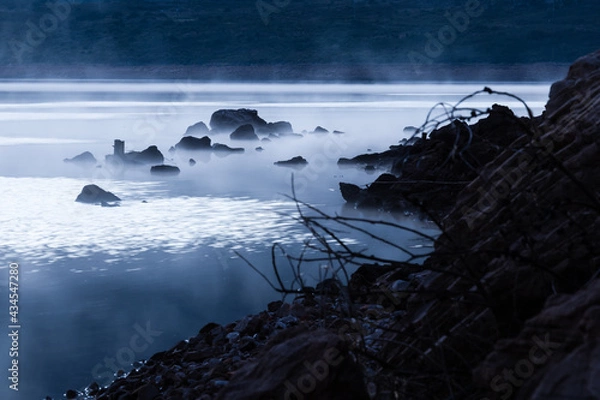Fototapeta Rocks in a lake or ocean scene sticking out above mist