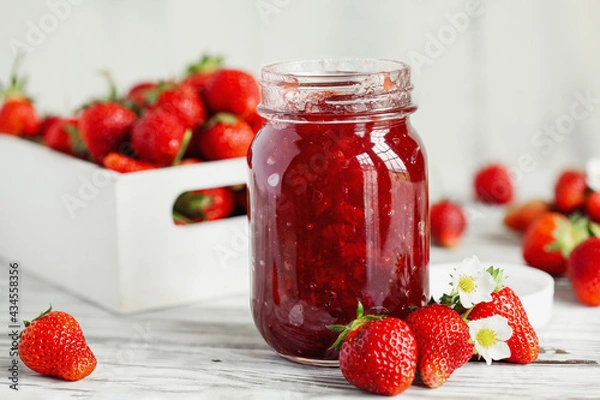 Fototapeta Homemade strawberry preserves or jam in a mason jar surrounded by fresh organic strawberries. Selective focus with blurred foreground and background.