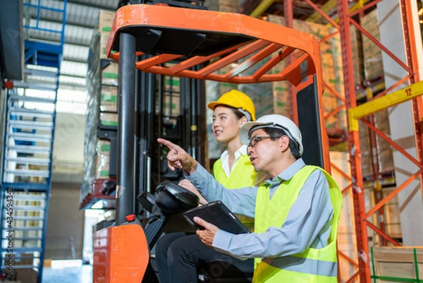 Fototapeta workers team meeting and training working at warehouse.Manager asian man standing with pointing check order with tablet.Female asia worker at large Warehouse in forklift loader