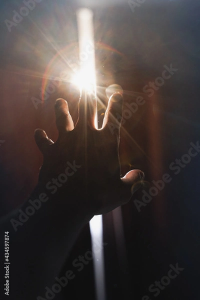 Fototapeta Art photo with a hand reaching for a strip of light between the curtains. Blurred image with backlight and highlights. From darkness to light concept.