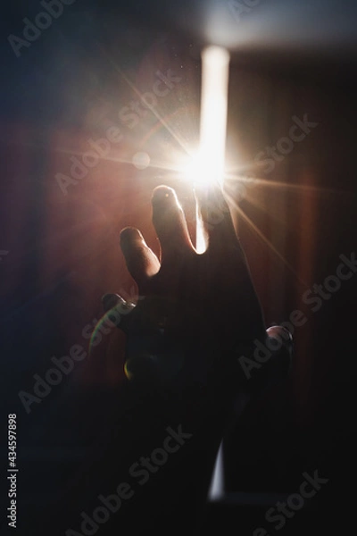 Fototapeta Art photo with a hand reaching for a strip of light between the curtains. Blurred image with backlight and highlights. From darkness to light concept.