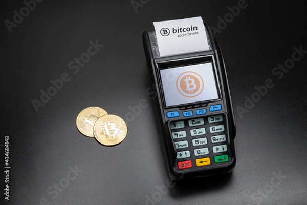 Fototapeta Payment terminal ready to accept bitcoins for payment. There are gold bitcoin coins on the black table nearby