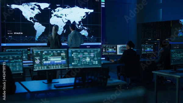 Fototapeta Project Manager Uses Digital Tablet Talks with Computer Scientist Looks at Big Screen Display Showing Infographics Global World Map Data. Telecommunications Control Control Room with People Working