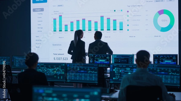 Obraz Project Leader, Chief Executive Discuss Data Shown on Big Display. Screens Show Infographics, Charts, Finance Analysis, Stock Market, Growth.Telecommunications Control Room with Working Professionals