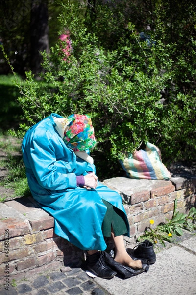 Obraz Old grandmother in a blue coat resting in the park, took off her shoes, tired legs