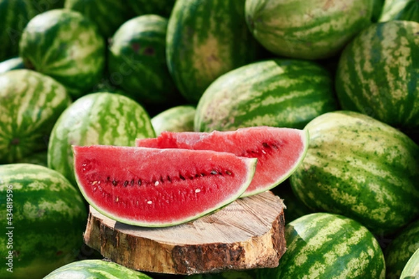 Obraz A juicy ripe watermelon, cut up, lies on a pile of other watermelons. Red watermelon looks delicious lying in the sun on other watermelons.
