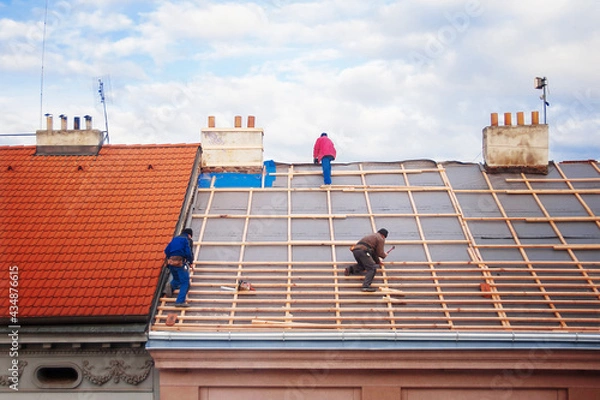 Obraz three builders replace the tiled roof in the old town
