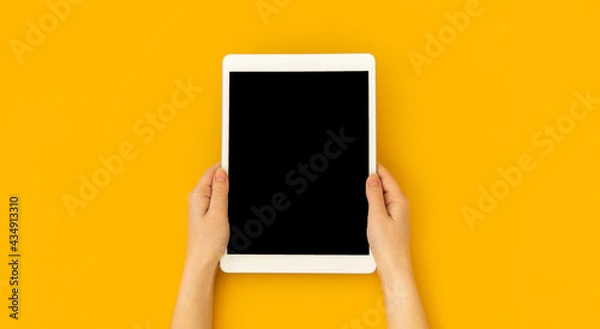 Obraz Woman hand holds digital tablet mockup with blank screen, education and application concept template, bright yellow background, top view and copy space photo