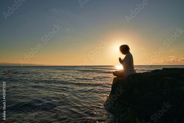 Obraz Silhouette of Peaceful woman meditating on a rock in the middle of a low wave sea at sunset time. golden hour colorr