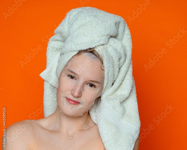 Fototapeta a girl with wet hair and a white towel on her head in a cosmetic mask with bare shoulders looks straight