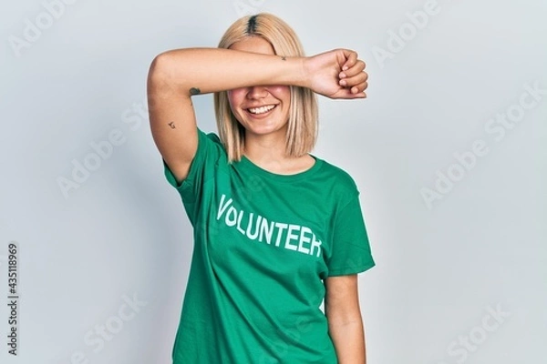Fototapeta Beautiful blonde woman wearing volunteer t shirt smiling cheerful playing peek a boo with hands showing face. surprised and exited