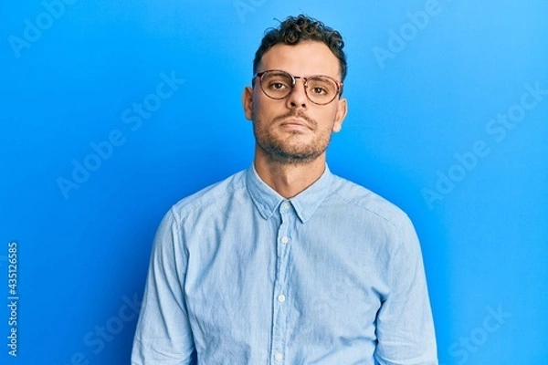 Fototapeta Young hispanic man wearing casual clothes and glasses looking sleepy and tired, exhausted for fatigue and hangover, lazy eyes in the morning.