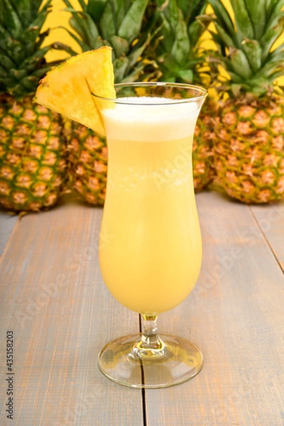 Obraz piña colada in a hurricane glass with a wedge of pineapple on top. made with white run, coconut cream, pineapple juice and ice. yellow bottom with fresh pineapples.