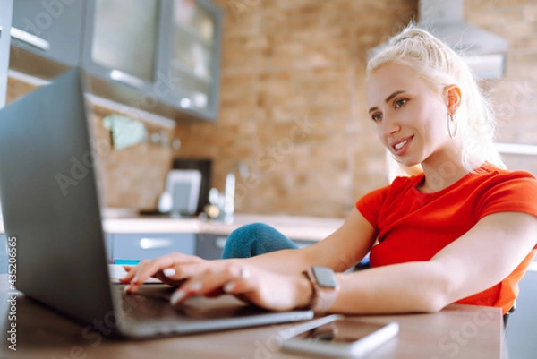 Fototapeta Young freelancer woman works and makes notes while working at home in quarantine lockdown. Social distancing. Self Isolation. Smiling woman working online or studying and learning while using notebook