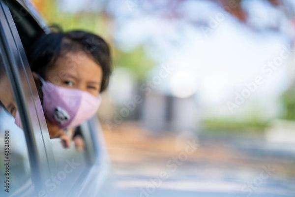 Fototapeta soft focus little girl sitting in car  wearing protective face mask against virus and pollutions.