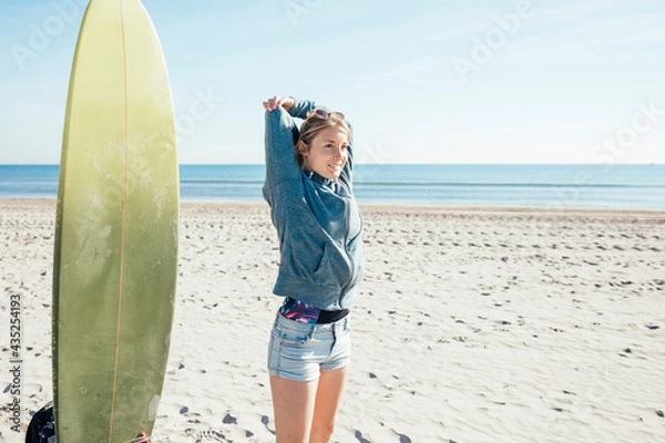 Fototapeta Surfer girl on the beach doing stretching before training.