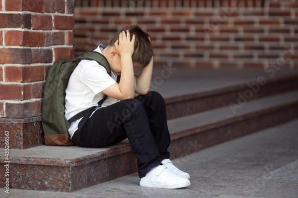 Fototapeta Upset boy sitting at school and crying after bullying by pupils classmates