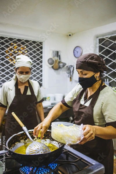 Obraz Vertical shot of two Hispanic women cooking chicken with mushroom sauce