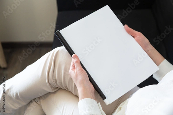 Obraz Hand holds white magazine with blank cover mock up. Hand in shirt hold clear magazine mockup template. A4 book softcover surface design.