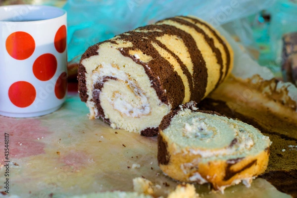 Fototapeta Cocoa roll with butter sliced on the table and a mug with red circles