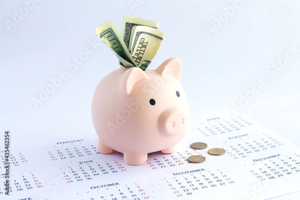 Obraz Piggy bank with dollars and coins on calendar, deposit or savings money concept
