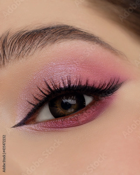 Fototapeta Beautiful macro shot of female eye make-up in pink smoky eyes style and arrow. Brown eye. Creative make-up. Perfect shape make-up and long lashes. Cosmetics. Beautiful eyes make-up. Close-up