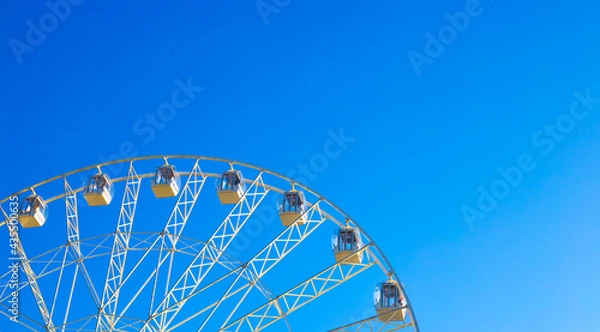 Obraz Panoramic ferris wheel carousel with cabins spinning against a blue sky, copy space. Summer fun in the amusement park