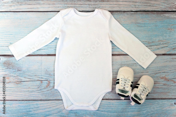 Obraz Top view white baby bodysuit with long sleeve on wooden background. Copy space for lettering or your text. Flat lay mockup. Stock photo. Styled stock photography