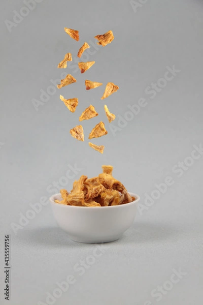 Obraz flying food concept - dried pineapple pouring into a bowl against gray background