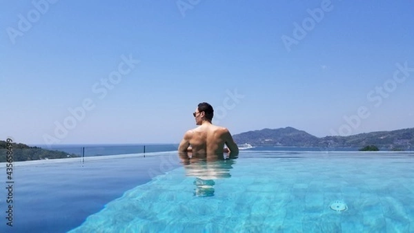 Fototapeta Muscular asian man relaxing in an infinity pool oceanside in a luxery resort sunbaking