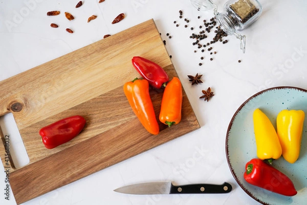 Fototapeta Background of food on a white marble table. Spices and knife on a wooden cutting board, top view, flat