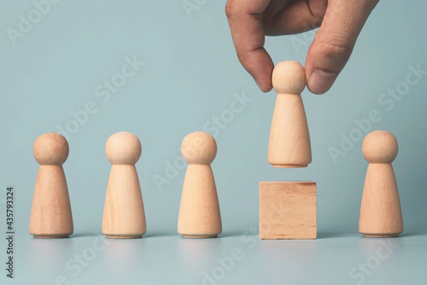 Fototapeta Hand putting wooden figure on wooden cube block on blue background , promotion to leadership and management growth concept.