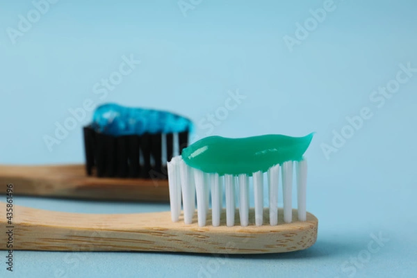 Fototapeta Wooden brushes with toothpaste on light blue background, closeup