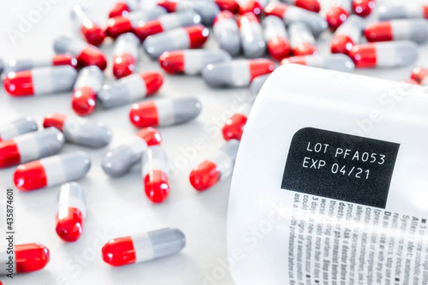 Fototapeta Expired date and lot number label print on medicine bottle with blurred background of pile of old red-grey painkiller pills on table, awareness expiration information from pharmaceutical manufacturing