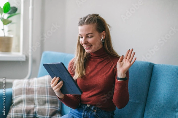 Fototapeta The girl communicates with family and friends by video call on the tablet. Chat and keep in touch without leaving home