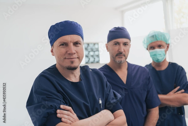 Fototapeta Multiethnic orthopedic doctor in front of his medical team looking at camera wearing face mask 