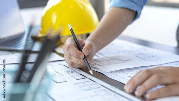 Fototapeta Engineer and Architect concept, Man uses a ruler to measure the floor plan on the blueprint, Building architecture design work, Construction design project under environmental conservation conditions.