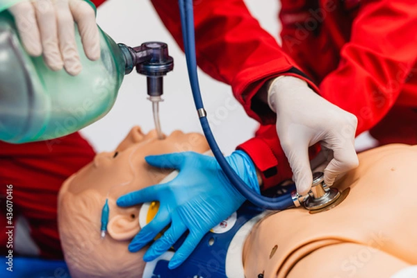Fototapeta Medic in latex gloves using CPR technique on dummy in first aid class. Oxygen mask on medical doll. Closeup