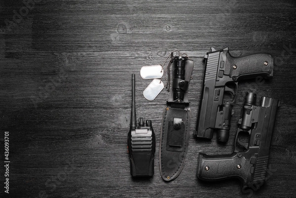 Fototapeta Black airsoft gun, walkie talkie radio station and knife and soldier badge on the black flat lay background with copy space.