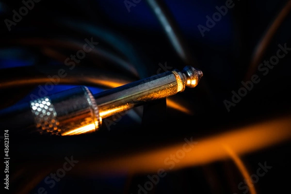 Fototapeta Macro Closeup of Tip on Quarter Inch Instrument Cable Connector Tangled in Cord on Blue Background with Orange Lighting