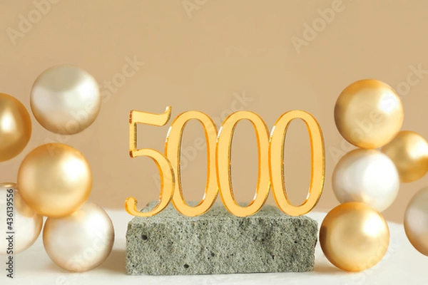 Obraz Number 5000 on a concrete podium and volumetric golden balls on a beige background. Copy space..