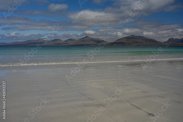 Fototapeta Shoreline at Luskentyre beach, Isle of Harris, Scotland. Sunny day with blue sky and clouds. White sand, turquoise sea, gentle wave, mountains in background. Copy space.