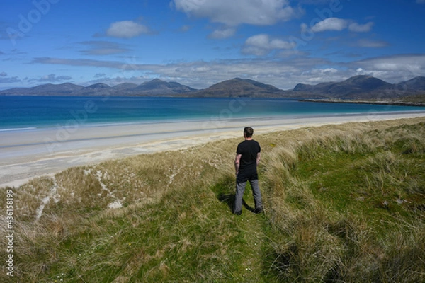 Fototapeta Man gazing out over white sands and turquoise water of Luskentyre beach in Isle of Harris, Outer Hebrides, Scotland. Mountains in background.